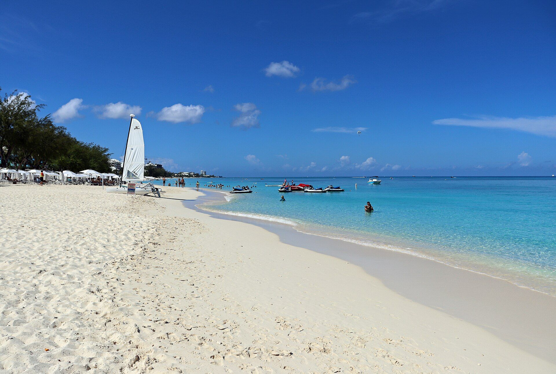 White sand and turquoise water stretching south along Seven Mile Beach, Grand Cayman, with a sailboat on the shore